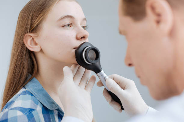 Examining face melanoma . Involved motionless young girl sitting in the clinic and enjoying appointment while dermatologist examining patient face skin and using dermatoscope