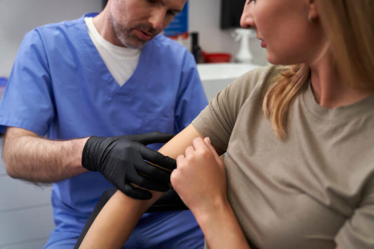 A dermatologist is examining a mark on a woman's arm to check for skin cancer.