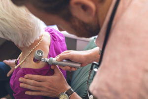 A male dermatologist is examining a senior patient using dermatoscopy to check for melanoma skin cancer.