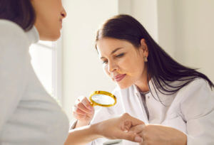Female dermatologist examining hand skin of a young woman patient using magnifying glass during a skin cancer screening.